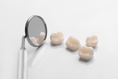 Zirconia crowns beside a dental mirror on a white surface